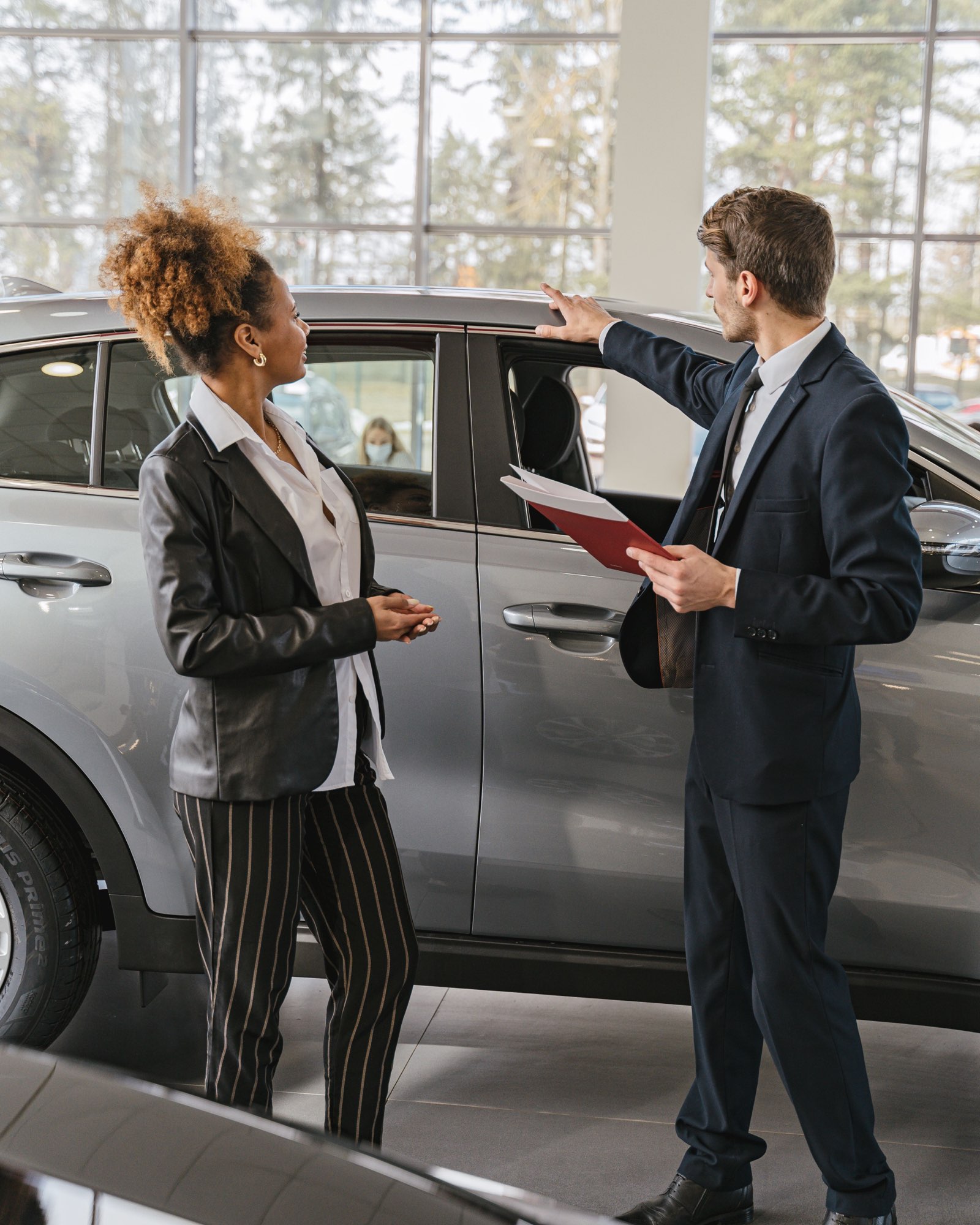 Vendedor y clienta conversando junto a un auto completo en el showroom de una concesionaria
